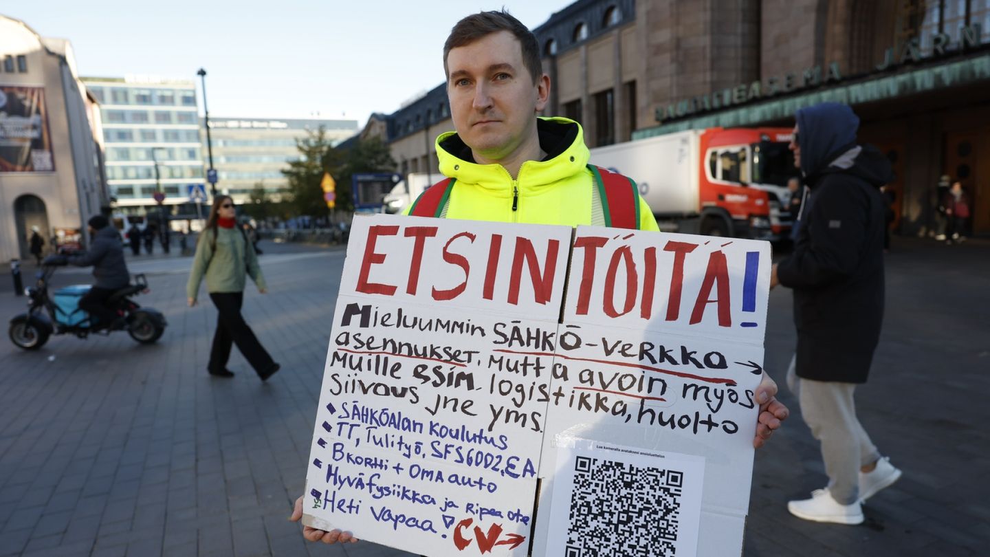 Työt | Aleksei Guliaev seisoo aamu­ruuhkassa kyltti kädessä, että saisi töitä